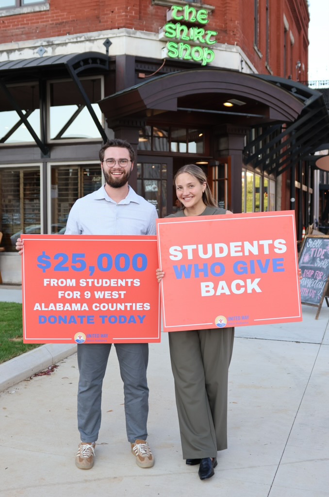 Garrett McNeil and Piper Larkin with United Way signs outside The Shirt Shop